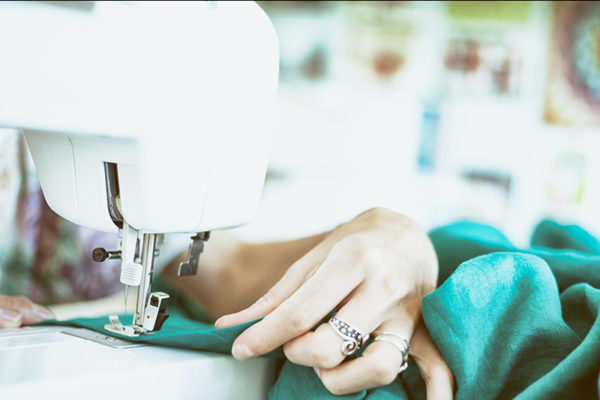 A hand pulls through bright teal coloured fabric through a sewing machine