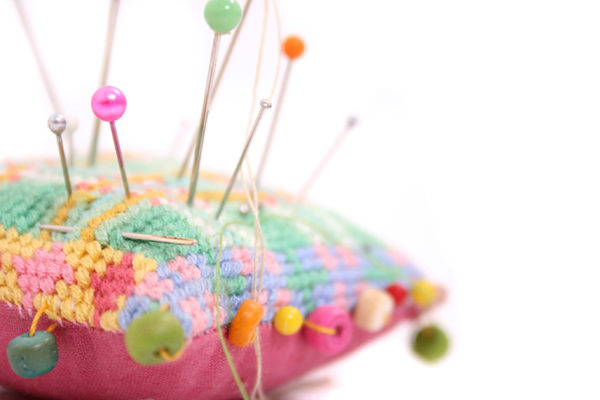 A colourful, embroidered pin cushion with pins and beads in assorted colours.