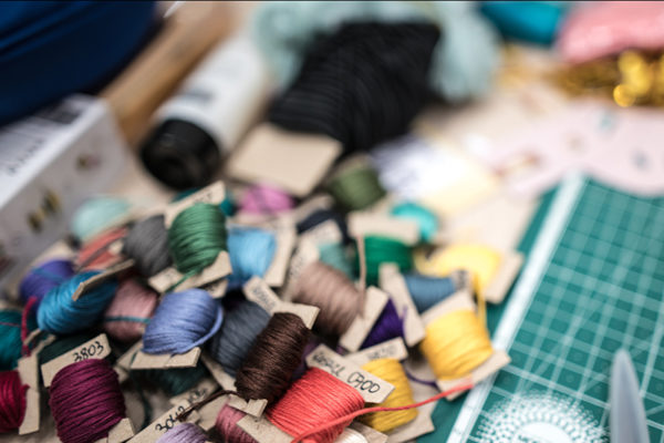 Spools of embroidery floss in many colours are piled beside a cutting board and scissors.