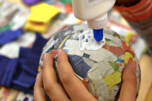 a close up view of someone glueing paper to a balloon for papier-mâché