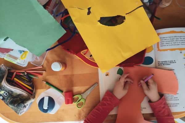 overhead view of a child drawing on orange construction paper with an array of art supplies on the table